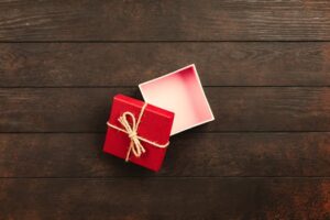 Top view of an open red gift box tied with twine on a wooden surface.