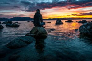 Silhouette of a man seated on rocks, gazing at a serene Lake Tahoe sunset.