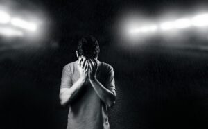 Black and white photo of a man covering his face, conveying emotion and solitude.