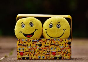 Two yellow smiley plush toys in an emoji-themed box, expressing fun and happiness.