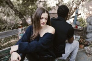 A couple sits on a bench back-to-back, conveying sadness and separation outdoors.