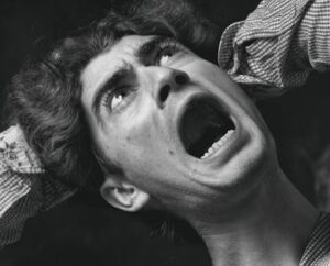 A dramatic black and white close-up of a man with an open mouth showing fear.