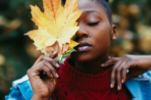 Close-up portrait of a woman holding a large autumn leaf outdoors.