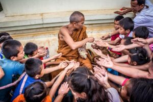 A Buddhist monk shares candies with a joyful group of children, fostering cultural connection and kindness outdoors.